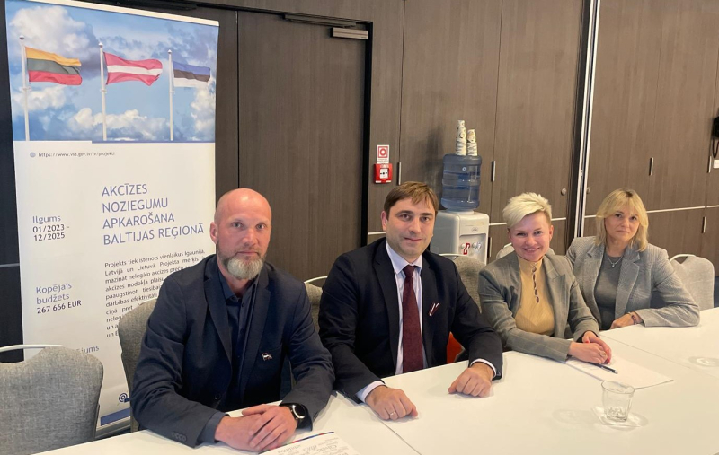 Divas sievietes un divi vīrieši pie galda oficiālā pasākumā 