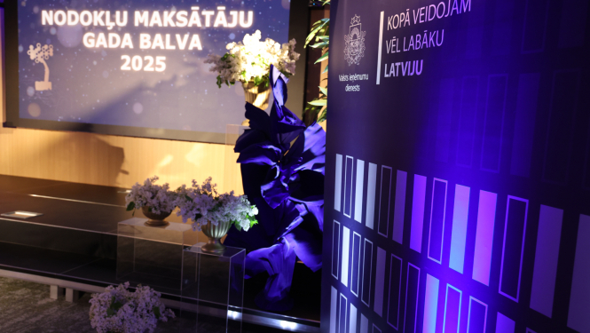 Banneris ar uzrakstu "Nodokļu maksāt'ju gada balva" ziedu dekorācijas