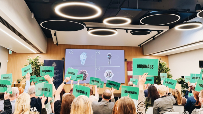 Konferenču zāle, skats uz ekrānu, cilvēki tur rokās zaļa fona lapas ar tekstiem