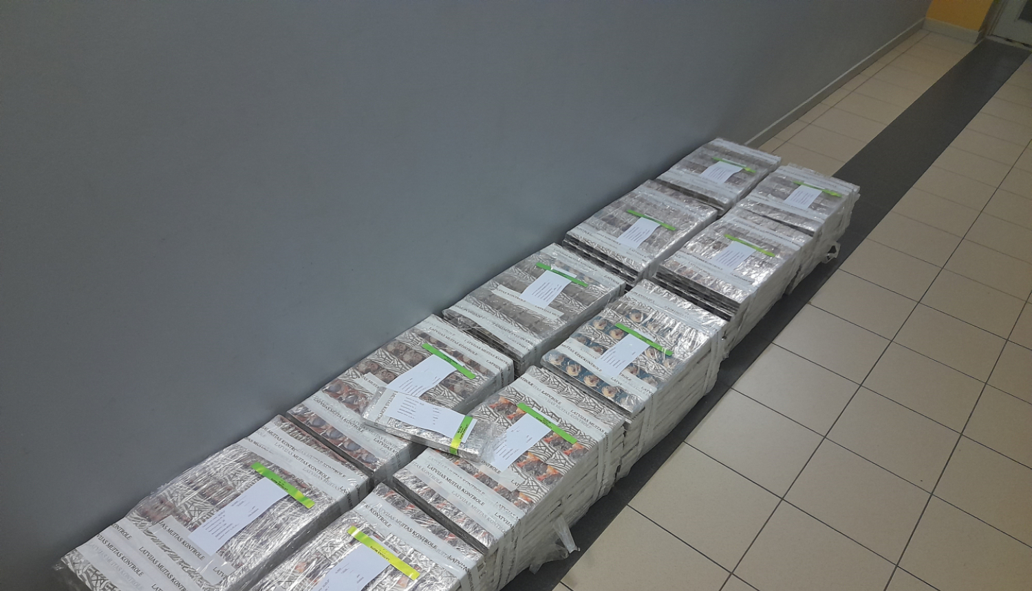 10 plēvē ietītu cigarešu iepakojumi salikti uz grīdas