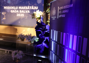 Banneris ar uzrakstu "Nodokļu maksāt'ju gada balva" ziedu dekorācijas