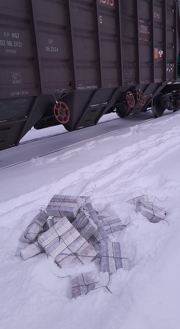 Blakus dzelzceļa vagonam sniegā stāv izņemtie iepakojumi ar kontrabandas cigaretēm.