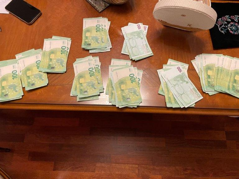 Uz galda vairākas kaudzītes ar 100 eiro banknotēm un mobilais telefons