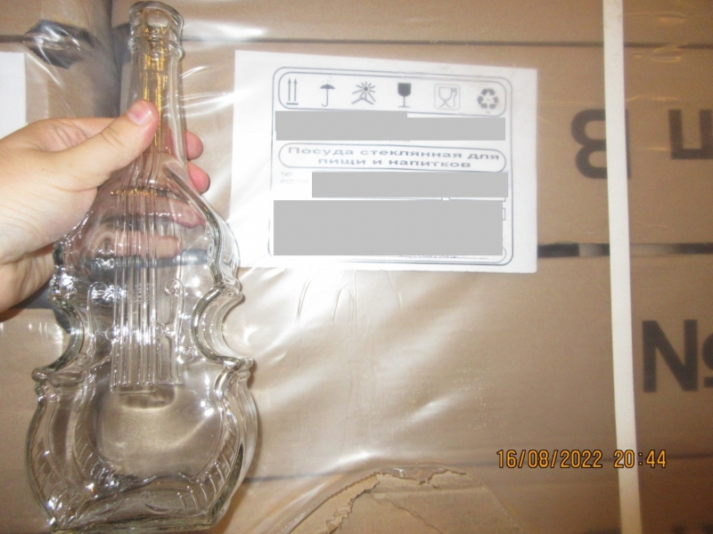 Stikla pudele vijoles formā uz kartona kastes ar aprakstošo etiķeti