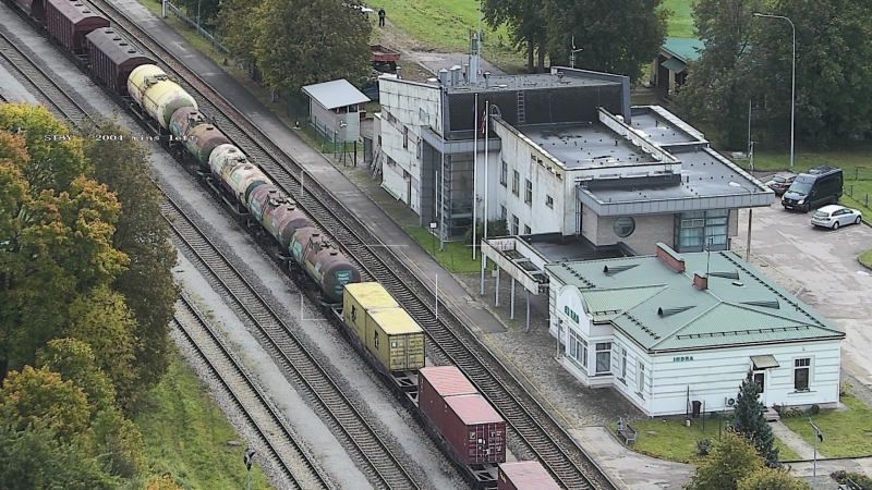 Kravas vilciena sastāvs uz sliedēm un stacijas ēka 