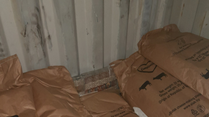 Pie vagona gala sienas aiz maisiem ar sauso pienu stāv paslēptas kontrabandas cigarešu paciņas