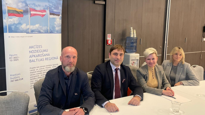 Divas sievietes un divi vīrieši pie galda oficiālā pasākumā 