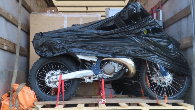 Daļēji ar melnu plēvi aptīts motocikls uz koka platformas  
