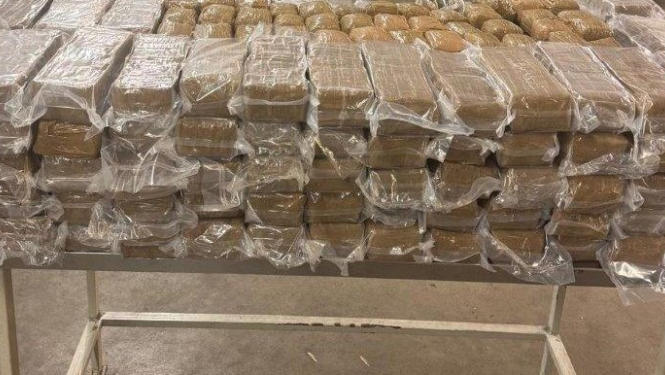 Uz galda salikts liels daudzums plēvē ietītu iepakojumu ar hašišu