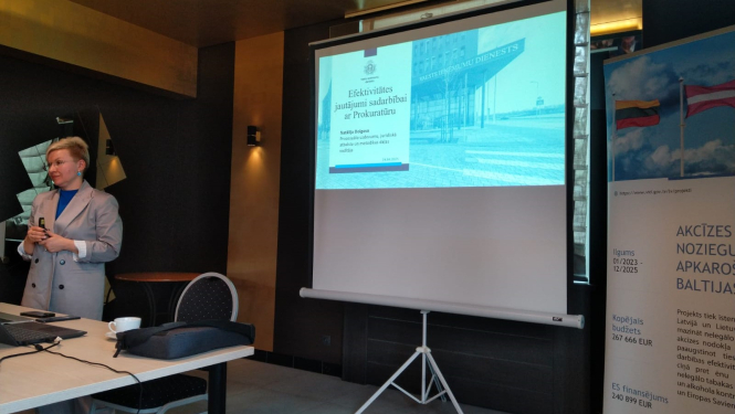 Sievete vada prezentācijiju, fonā ekrāns un banneris