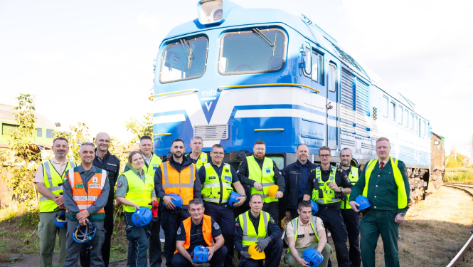 Muitas dienestu pārstāvju  grupas kopbilde uz zila vilciena vagona fona