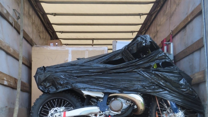 Daļēji ar melnu plēvi aptīts motocikls uz koka platformas  