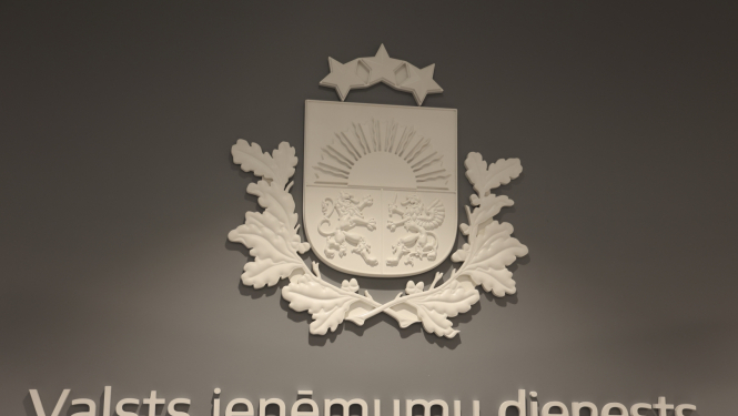 Balts ģērbonis un uzraksts Valsts ieņēmumu dienests uz pelēkas sienas