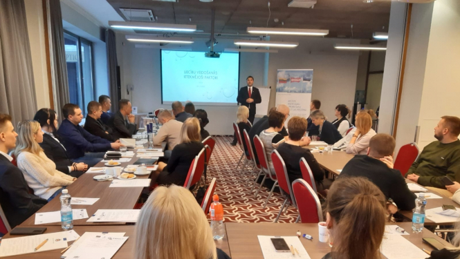 Priekšplānā cilvēki sēž pie galdiem