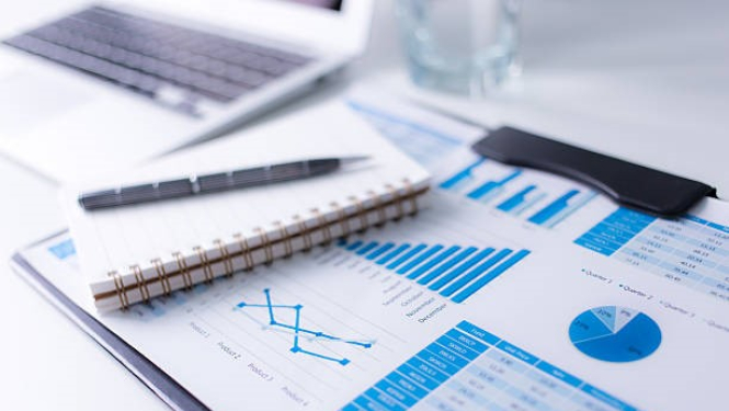 Uz galda bloknots ar pildspalvu un attēls ar diagrammām