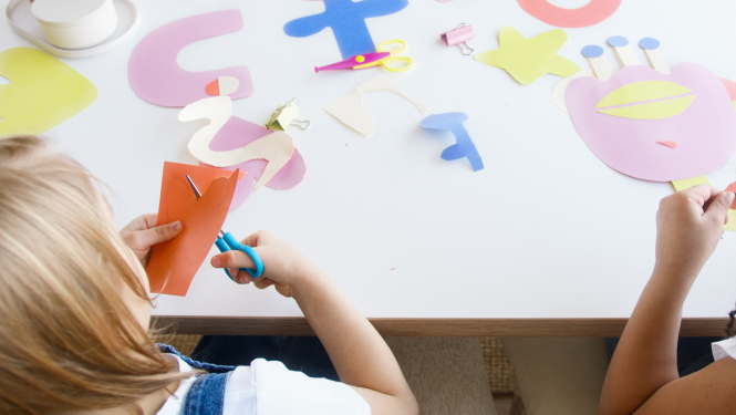 Bērns ar šķērēm griež aplikācijas papīru