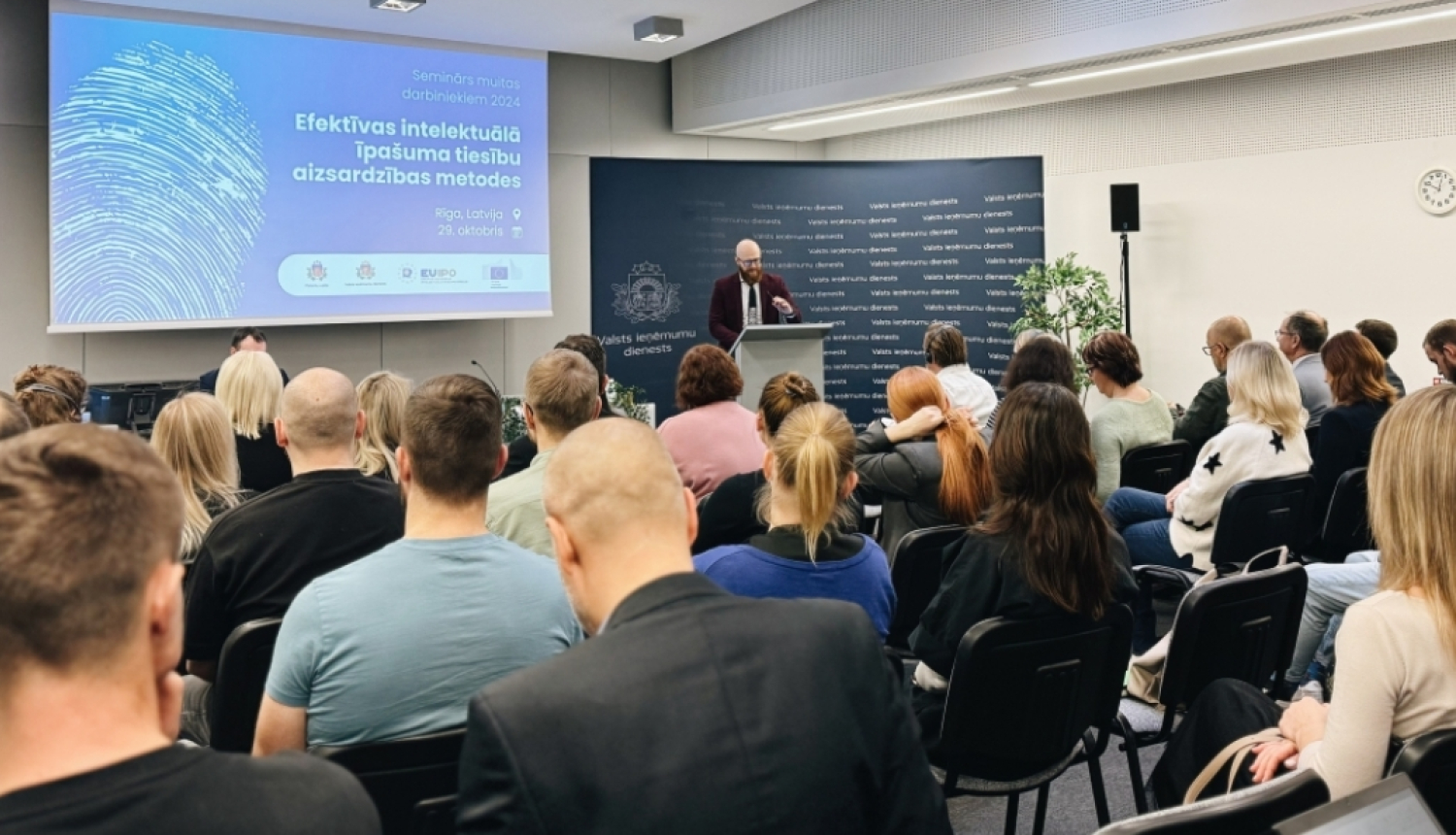 Patentu valdes foto: zālē sēž cilvēki priekšā stāv lektors