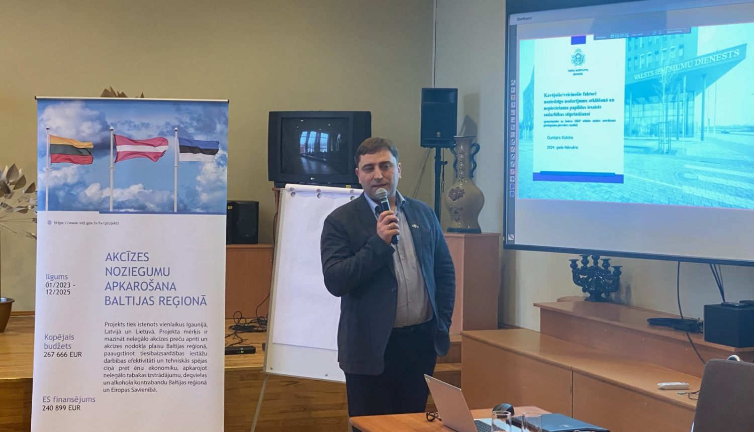 Nodokļu un muitas policijas direktors pie banera runā mikrafonā 