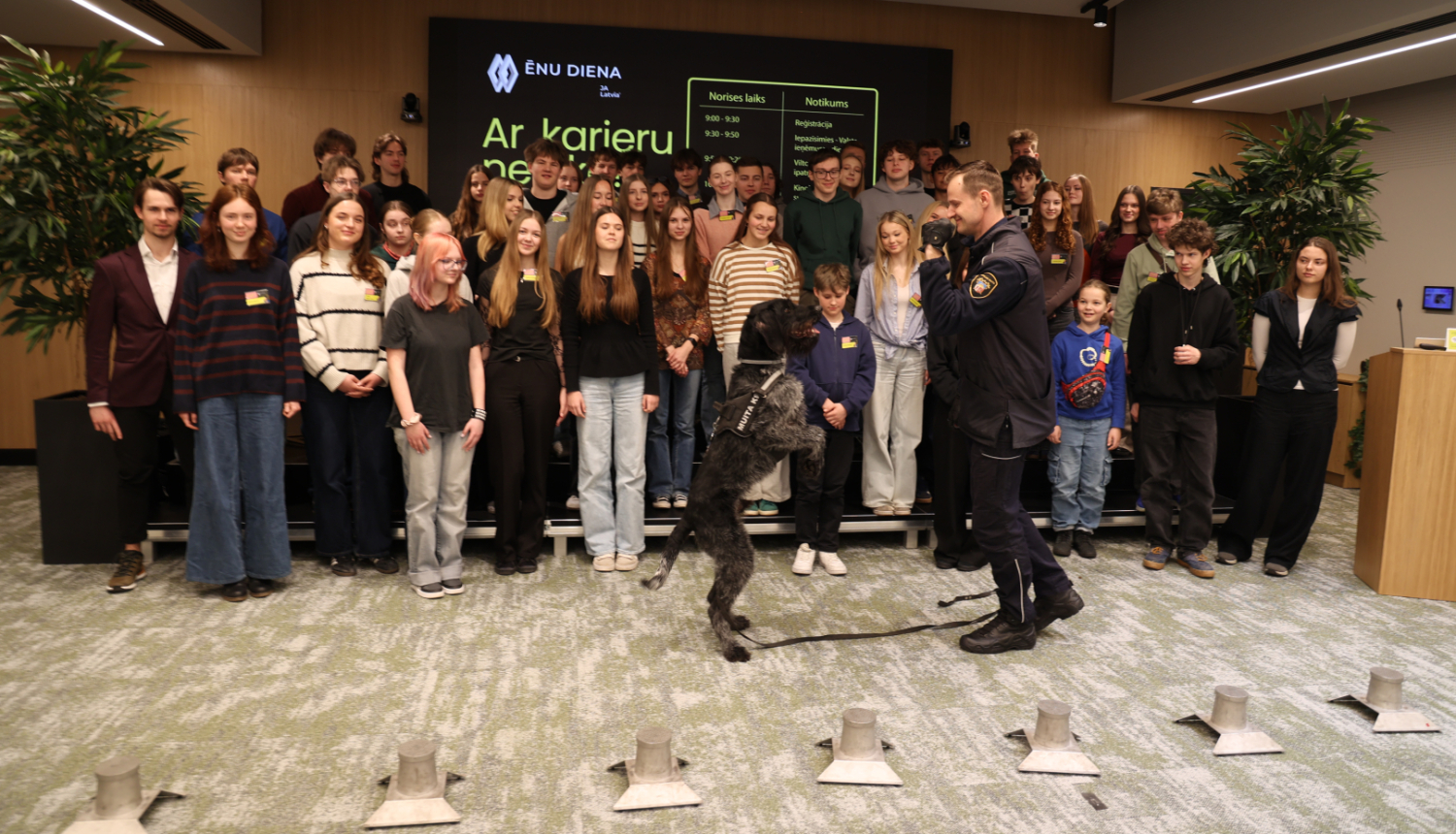 Ēnu dienas dalībnieku kopbilde, priekšplānā kinologs ar savu darba suni