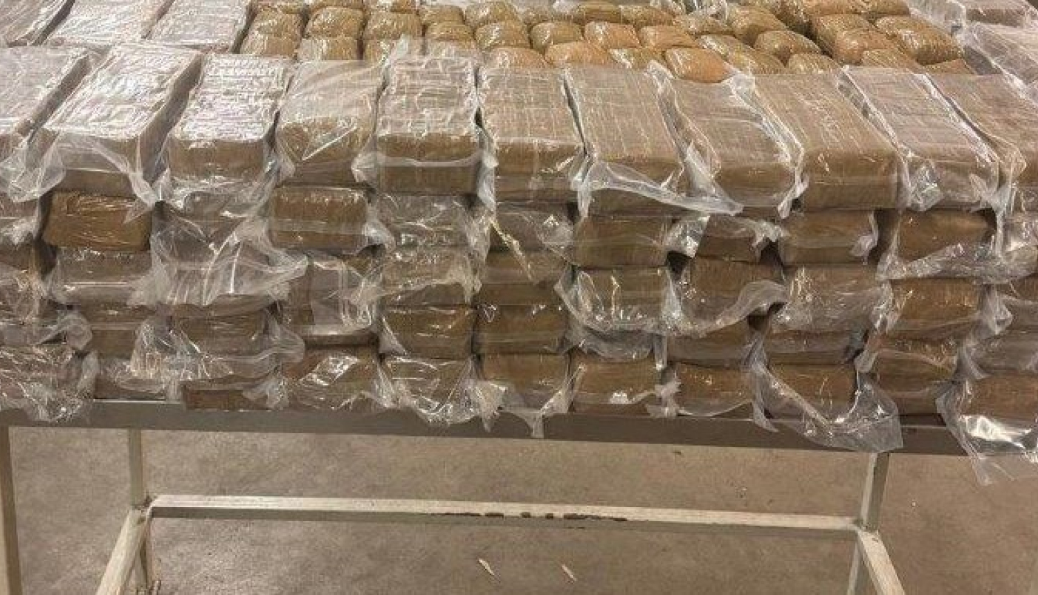 Uz galda salikts liels daudzums plēvē ietītu iepakojumu ar hašišu