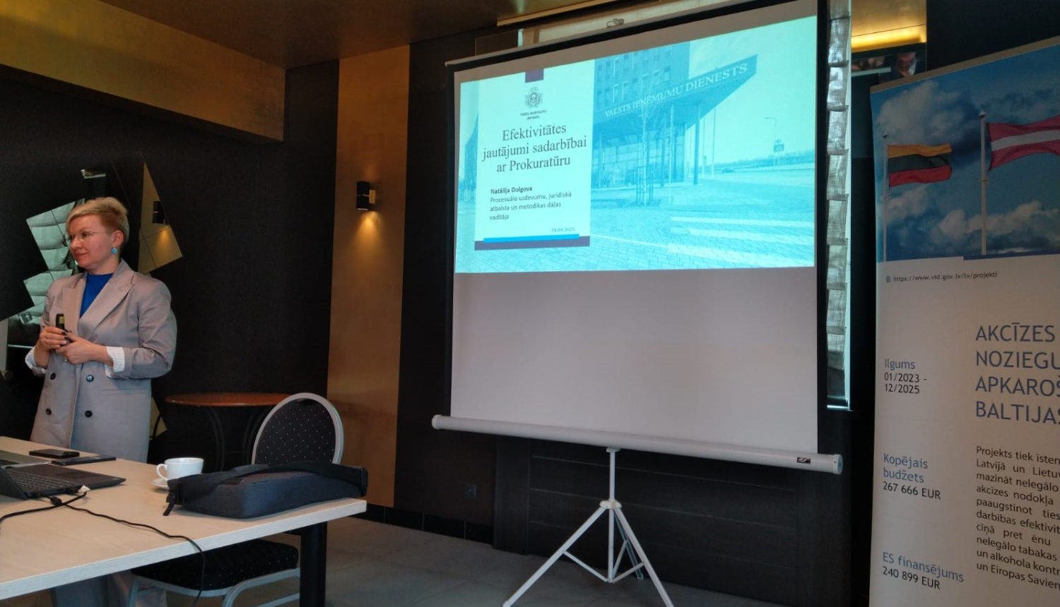 Sievete vada prezentācijiju, fonā ekrāns un banneris