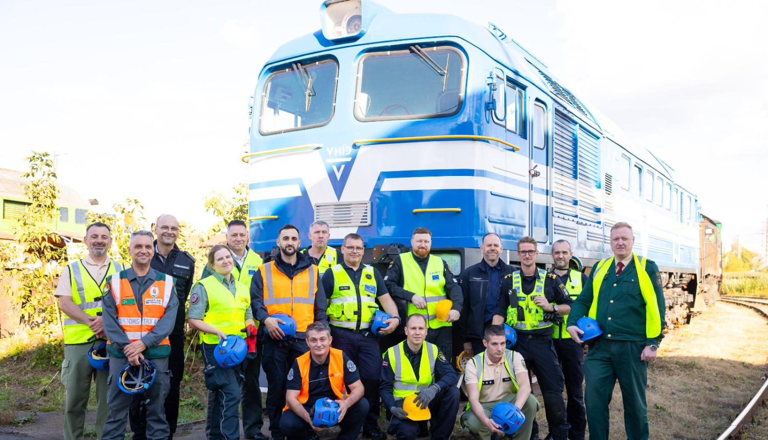 Muitas dienestu pārstāvju  grupas kopbilde uz zila vilciena vagona fona