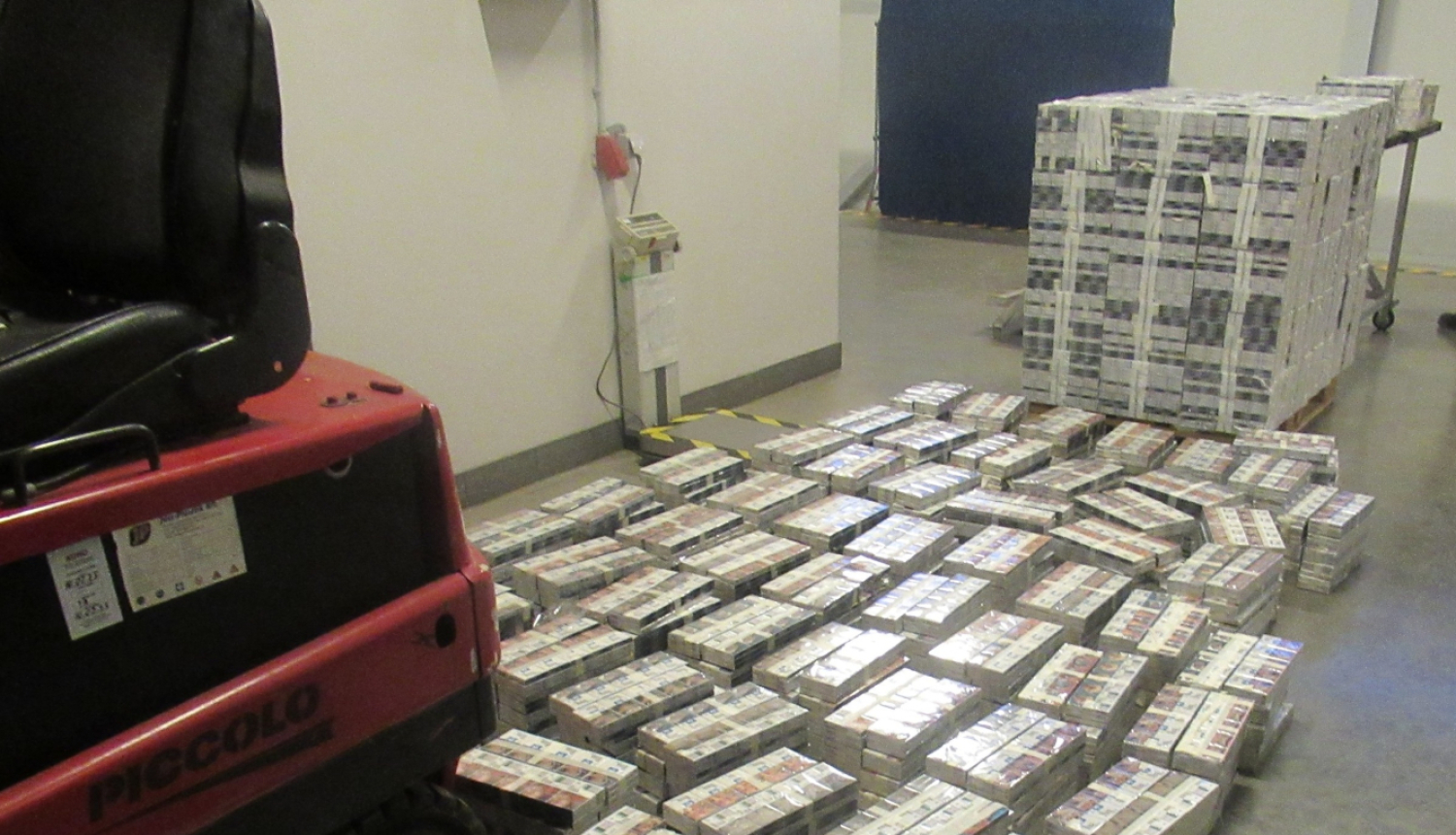 Uz grīdas kaudzēs sakārtoti daudz cigarešu bloki 