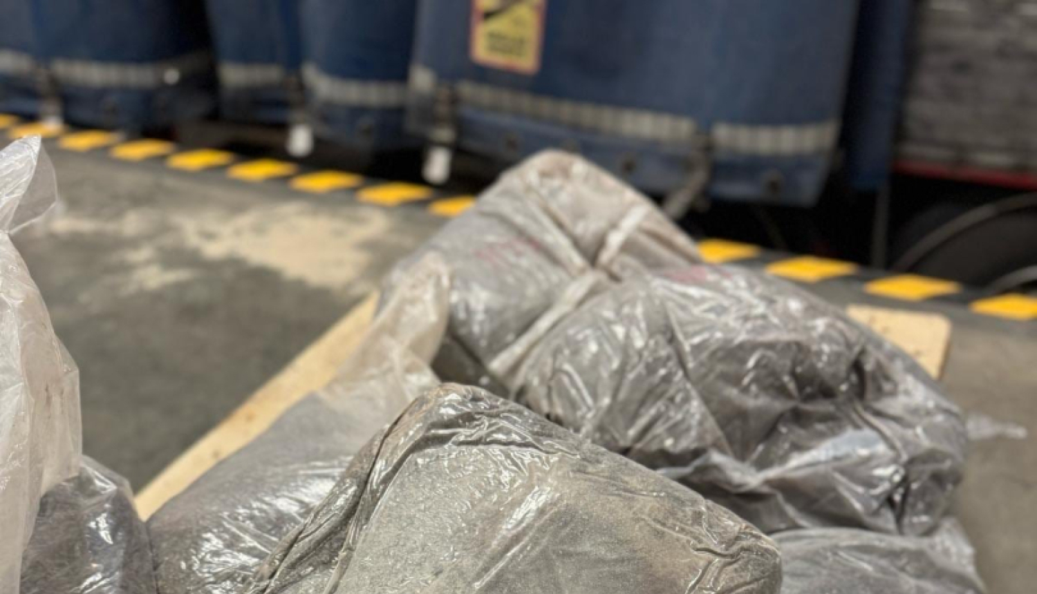 Tuvplānā redzami plēvē ietīti vairāki iepakojumi ar tumšu vielu 