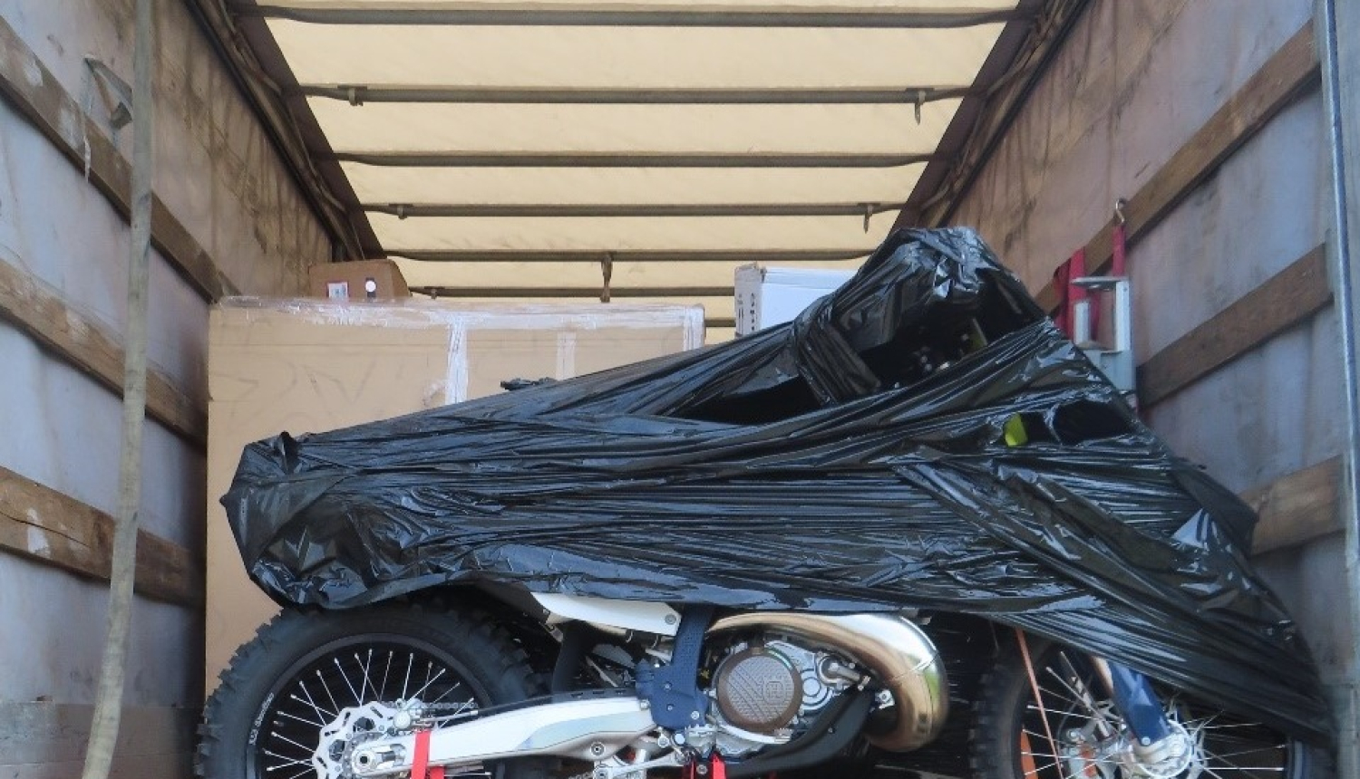 Daļēji ar melnu plēvi aptīts motocikls uz koka platformas  