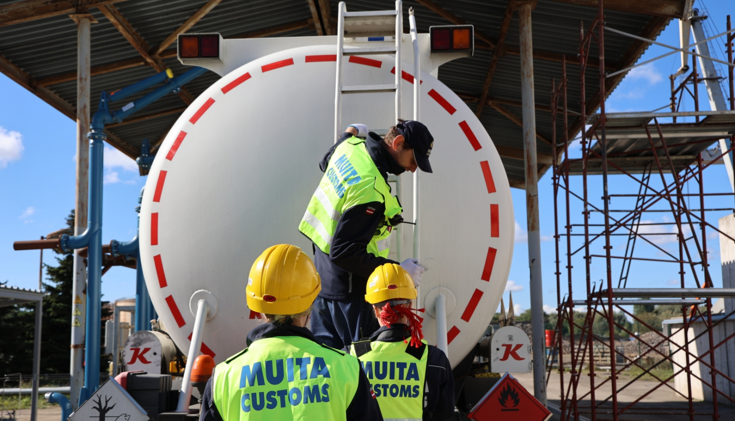 Trīs muitas darbinieki no aizmugures pie cisternas