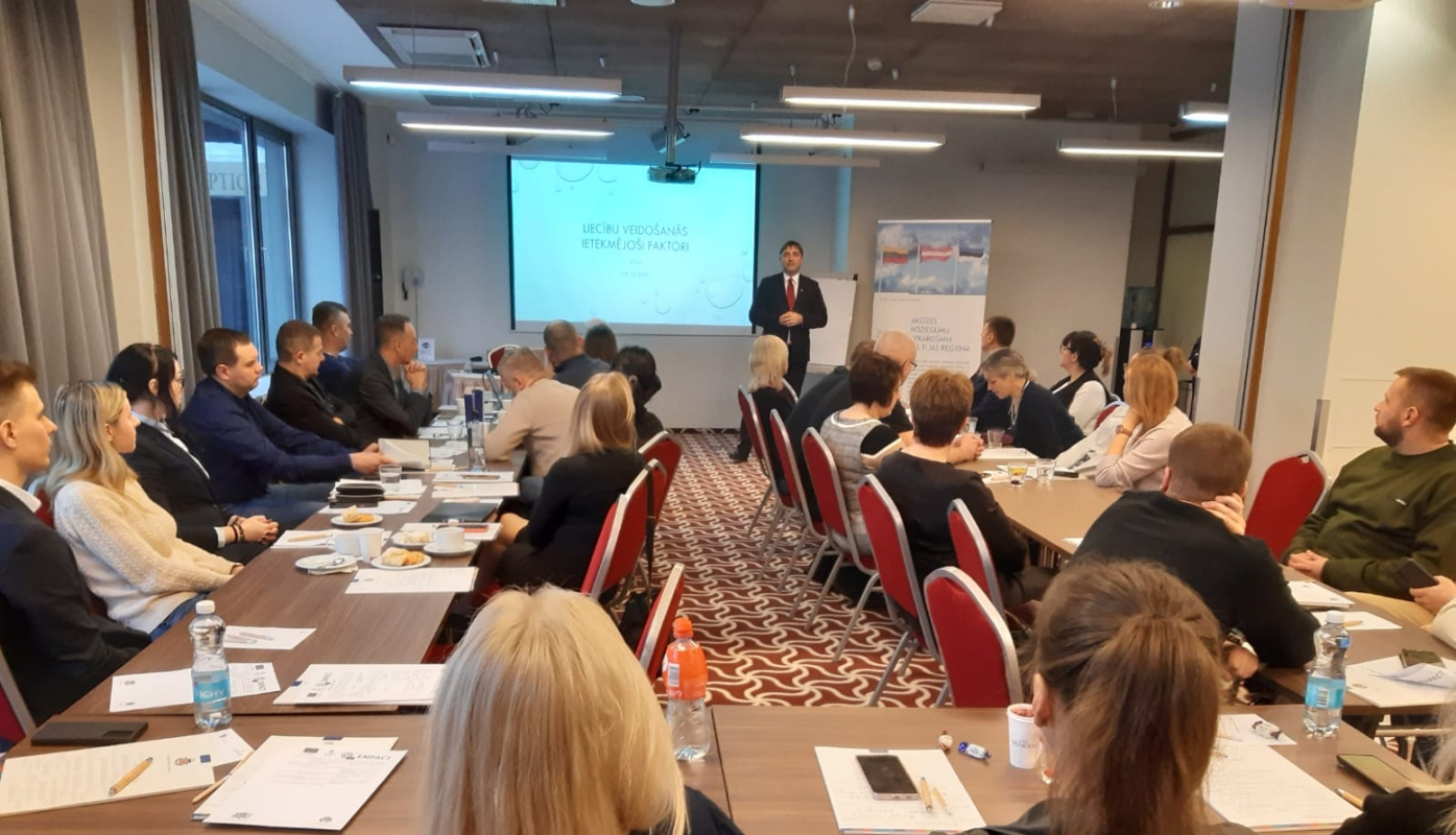 Priekšplānā cilvēki sēž pie galdiem