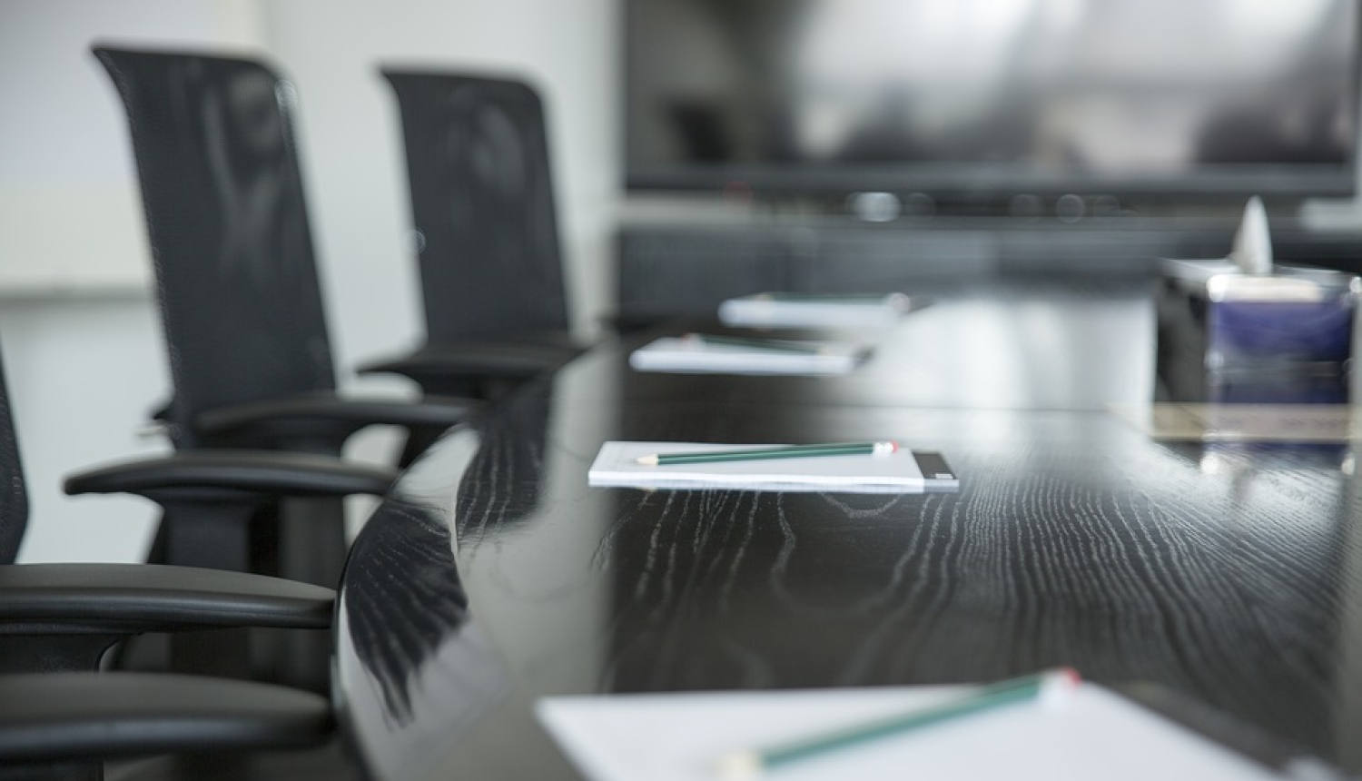 Krēsli pie galda, uz kura stāv piezīmju bloknoti ar zīmuļiem