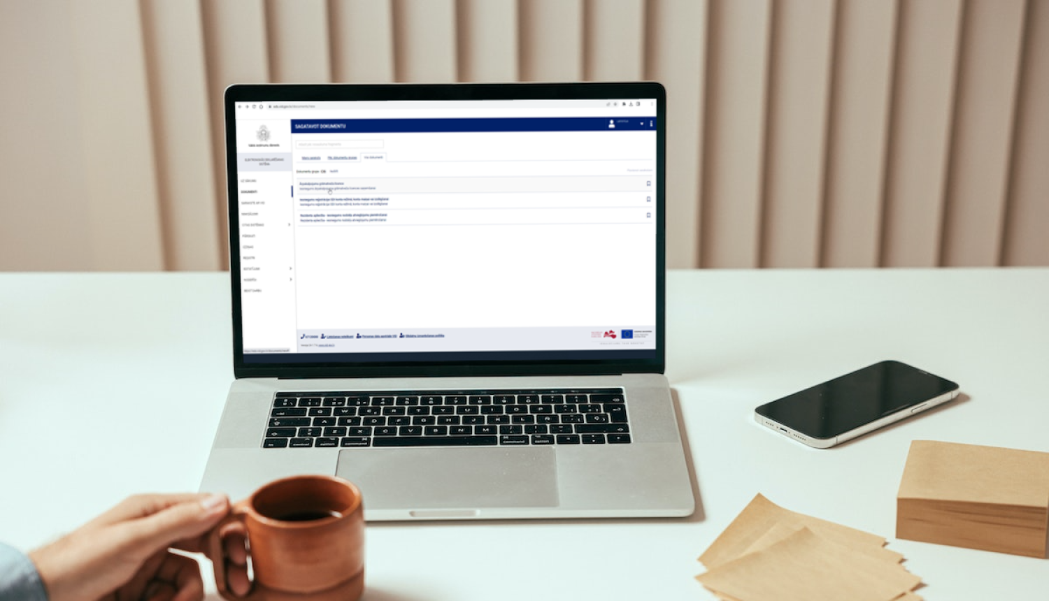 Uz galda novietots atvērts portatīvais dators, viedtālrunis un piezīmju lapiņas