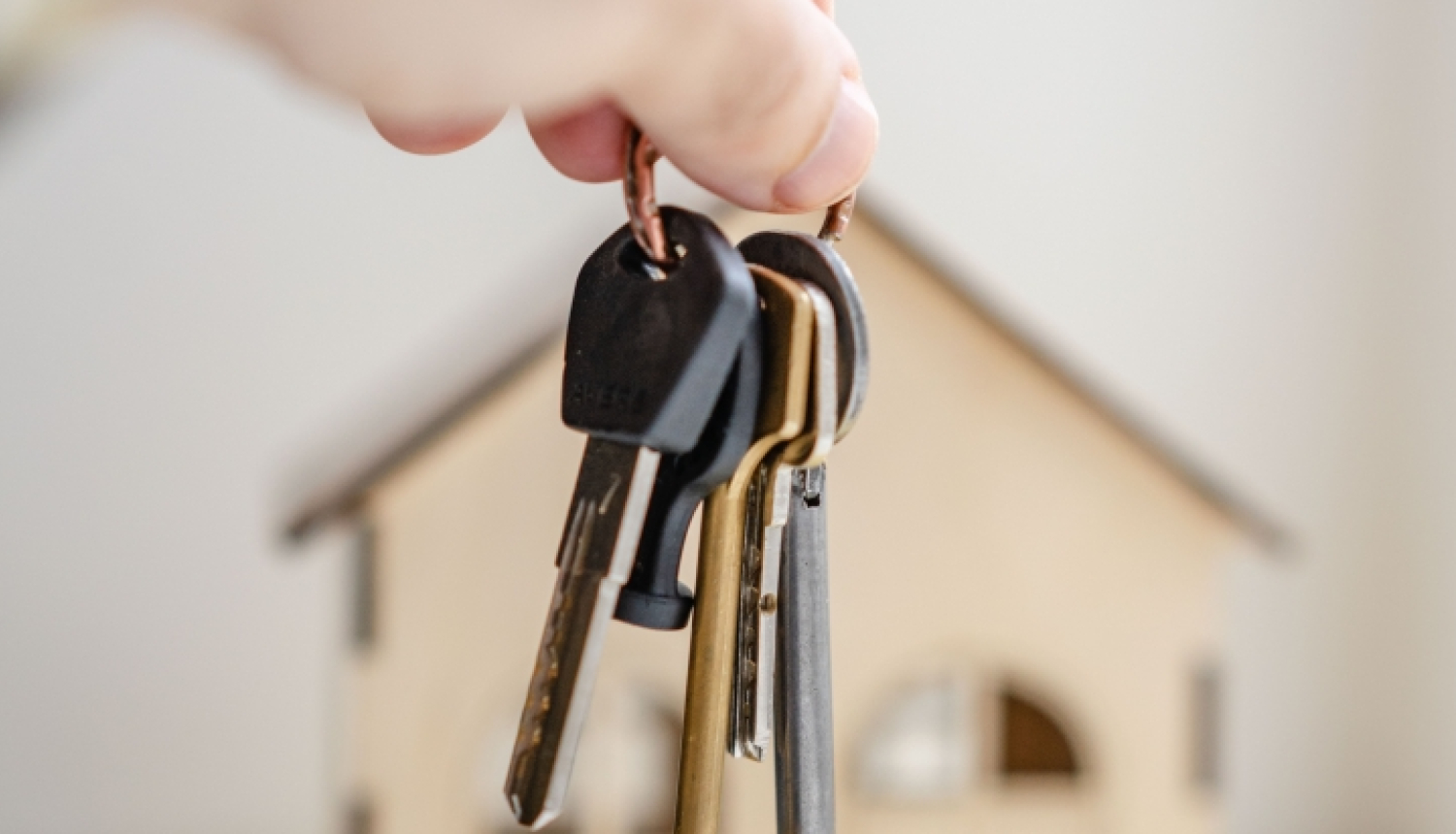 Rokā paņemts atslēgu saišķis, fonā mājas makets