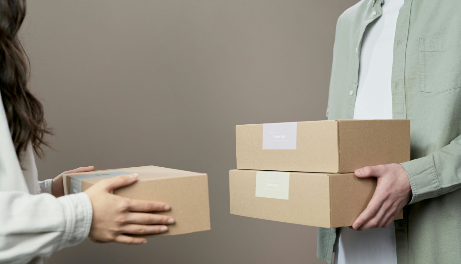 Divi cilvēki, tuvplānā rokās kartona kastes. 