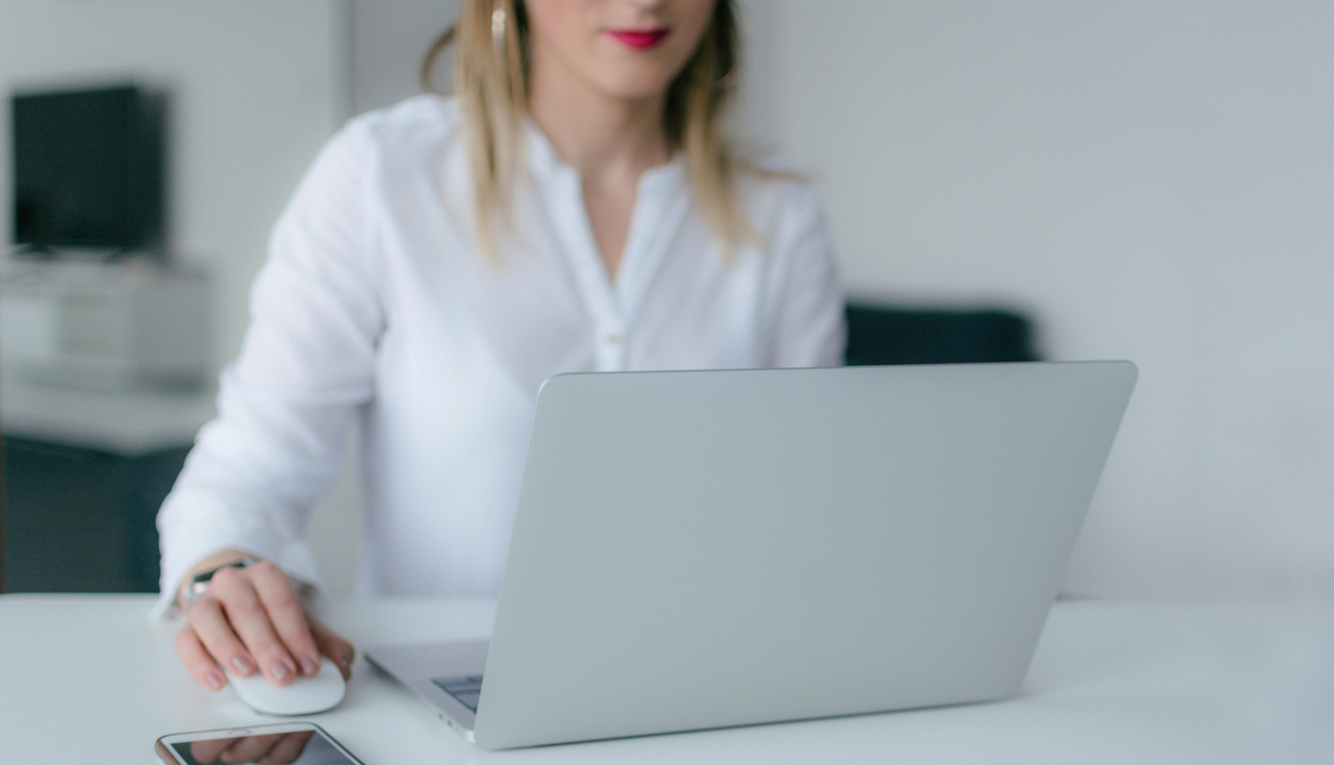 Sieviete sēž pie portatīvā datora, blakus mobilais telefons 