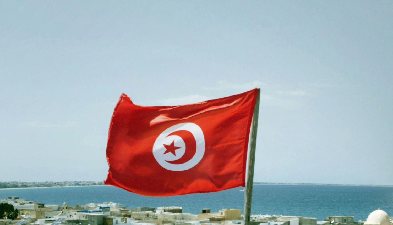 Tunisijas karogs fonā krasta līnija ar skatu uz ūdeni