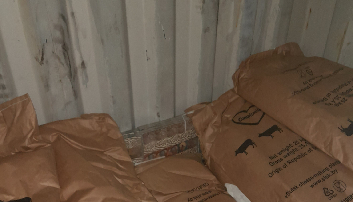 Pie vagona gala sienas aiz maisiem ar sauso pienu stāv paslēptas kontrabandas cigarešu paciņas