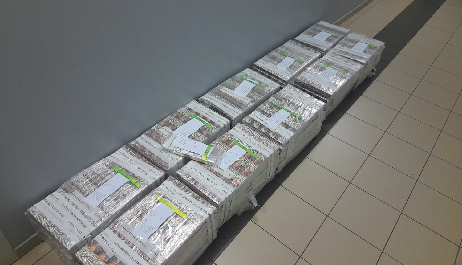 10 plēvē ietītu cigarešu iepakojumi salikti uz grīdas