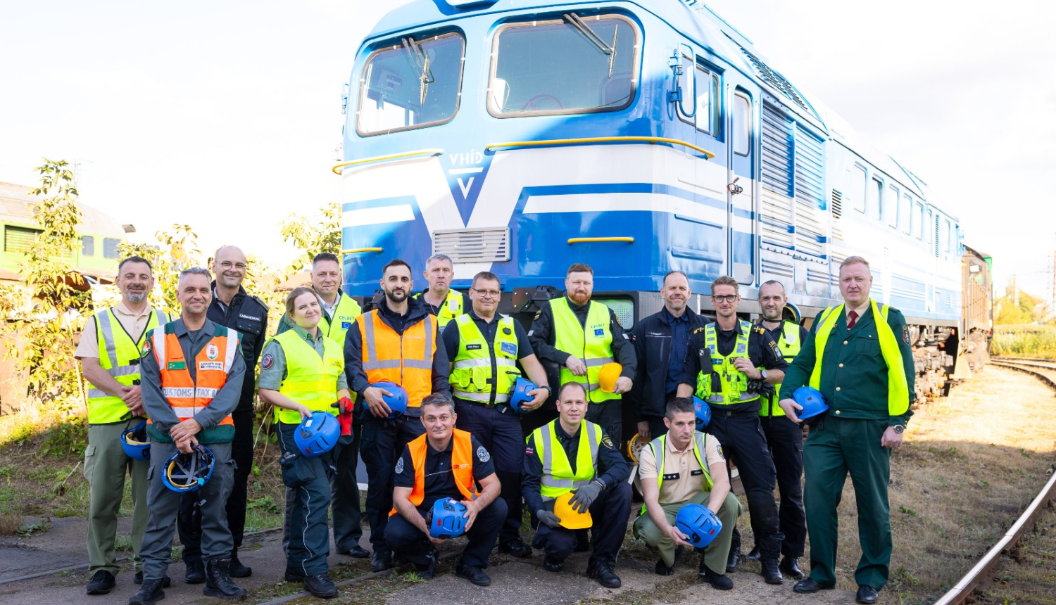 Muitas dienestu pārstāvju  grupas kopbilde uz zila vilciena vagona fona