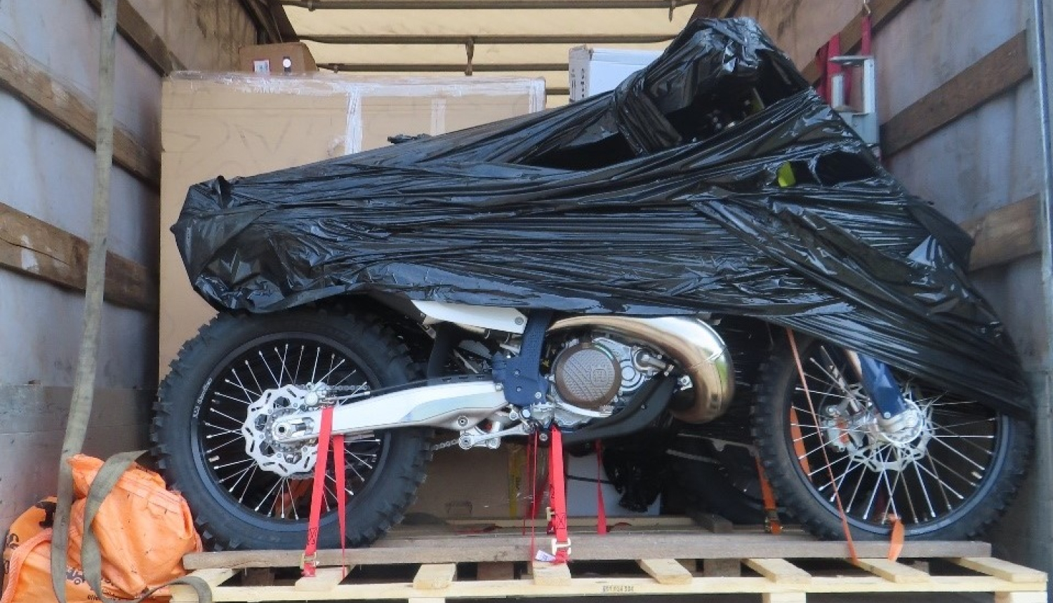 Daļēji ar melnu plēvi aptīts motocikls uz koka platformas  